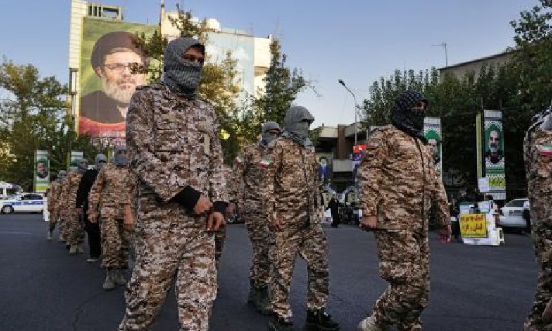 כוחות בסיג' רעולי פנים כשברקע שלט עם תמונותיהם של יחיא סינוואר, והאשם ספי א-דין בכיכר פלשתין בטהרן [צילום: ואחיד סלמי/AP]