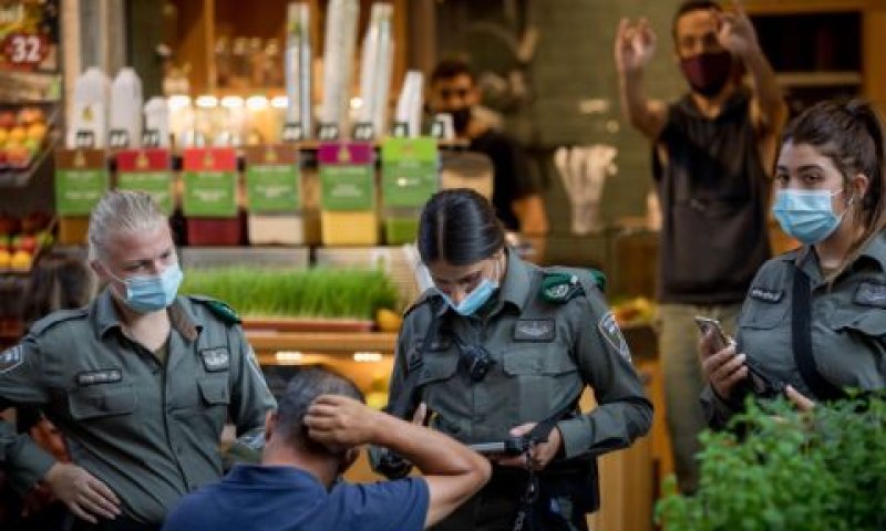 שוטרות מג"ב מבצעות אכיפה בירושלים ומאחוריהן אדם הנראה מסמן אצבע משולשת [צילום: נתי שוחט/פלאש 90]