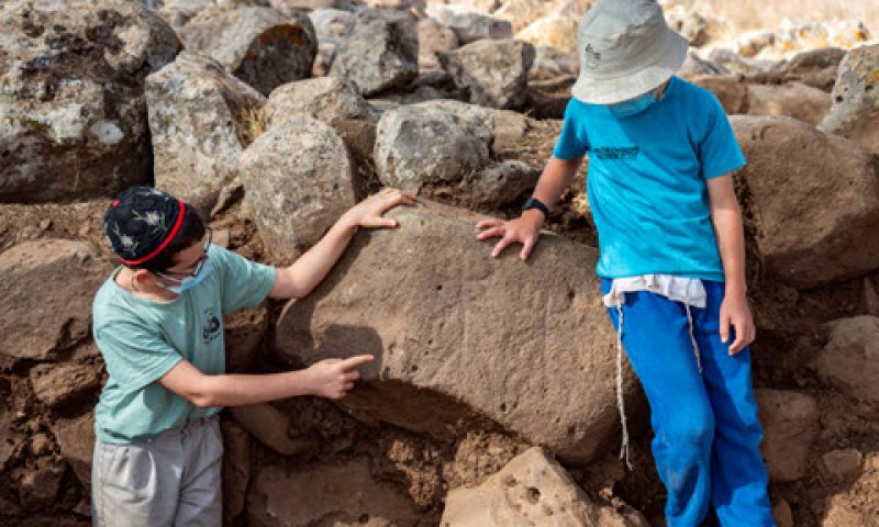 ילדים מחיספין המתנדבים בחפירה, מצביעים על הדמויות שחרותות על האבן [צילום: יניב ברמן, רשות העתיקות]