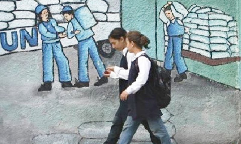 ילדות פלשתיניות חולפות על פני גרפיטי המתאר את הפעילות ההומינאטרית של האו"ם בעזה [צילום: AP]